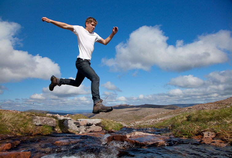 Boy (aged 17) jumping across upland stream, Cairngorms National Park, Scotland, August